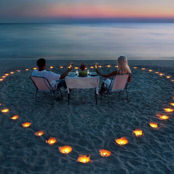 Couple having dinner on the beach with candles arranged in a heart